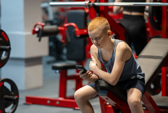 Ung dreng kigger på telefon i fitnesscentret